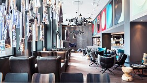 A modern lounge area with leather seating, a bar, and a large screen. - Motel One Basel (Basel)