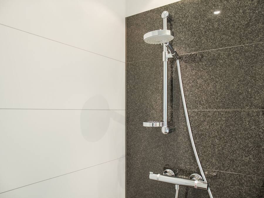 Una ducha moderna con cabezal de ducha de mano y panel de control en la pared.