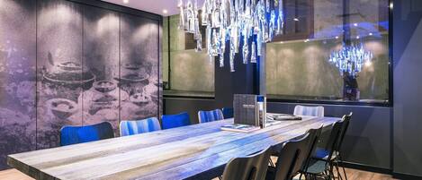 A modern conference room with a long table, blue chairs, and a chandelier.