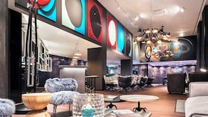 A modern lounge area with a bar, seating, and artwork on the walls. - Motel One Basel (Basel)
