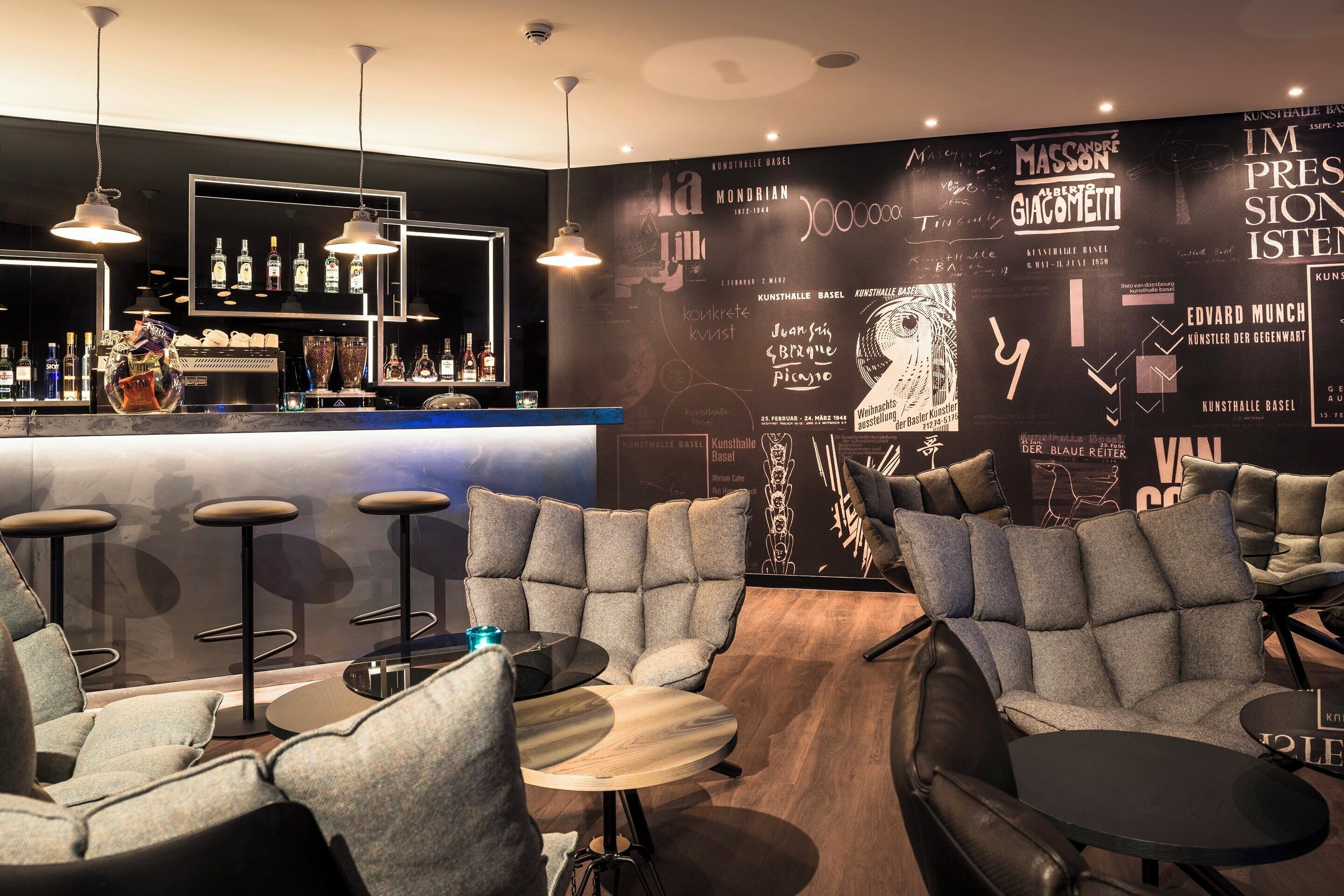 A bar area with stools, a counter with bottles, and a wall with art and text.