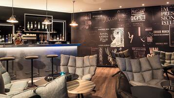 Una zona de bar con taburetes, una barra con botellas y una pared con arte y texto.