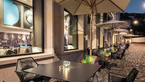 An outdoor seating area with tables and chairs, large umbrellas, and a view of the street. - Motel One Basel (Basel)