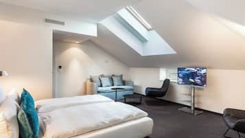 Une chambre d’hôtel moderne avec une lucarne, un lit avec du linge de maison blanc, un canapé, une télévision et un bureau.