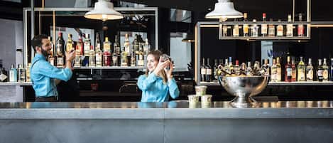 A bar area with a bartender and a customer, a large metal bowl, and shelves stocked with liquor bottles.