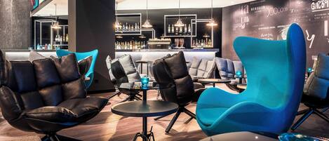 A modern lounge area with leather and blue chairs, a bar with various bottles, and a wall with text and images.