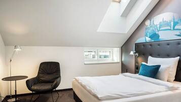 A hotel room with a bed, a chair, a lamp, and a window.