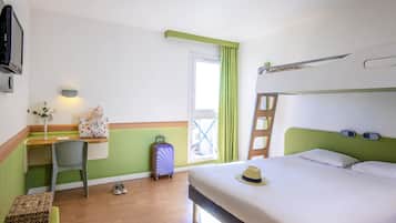 Une chambre d’hôtel avec un lit superposé, un bureau avec une chaise, une valise, un chapeau et un petit tabouret.