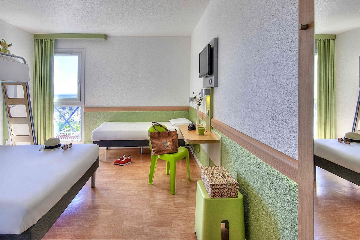 A hotel room with a bed, a desk with a chair, a television, and a window with curtains.