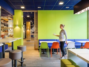 Una cafetería moderna con una pared verde brillante, detalles de madera y diversas opciones de asientos, incluyendo sillas y mesas.