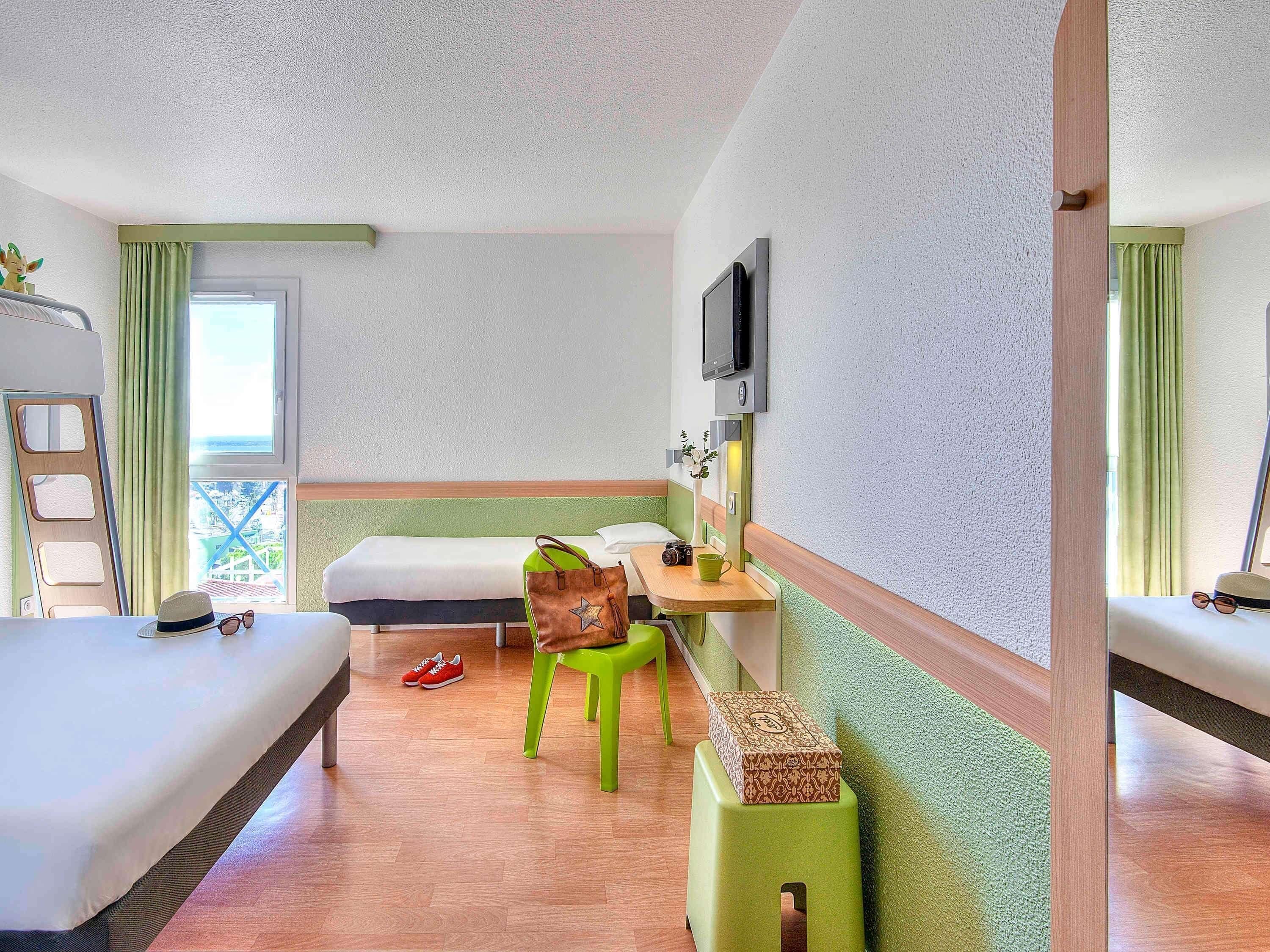 A room with two beds, a desk with a chair, a television, and a window with curtains.