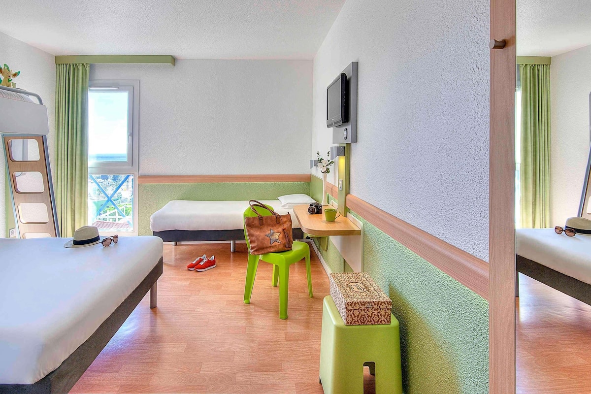 A room with two beds, a desk with a chair, a television, and a window with curtains.