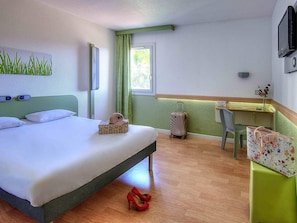 A hotel room with a bed, a desk, a chair, and a window with curtains.