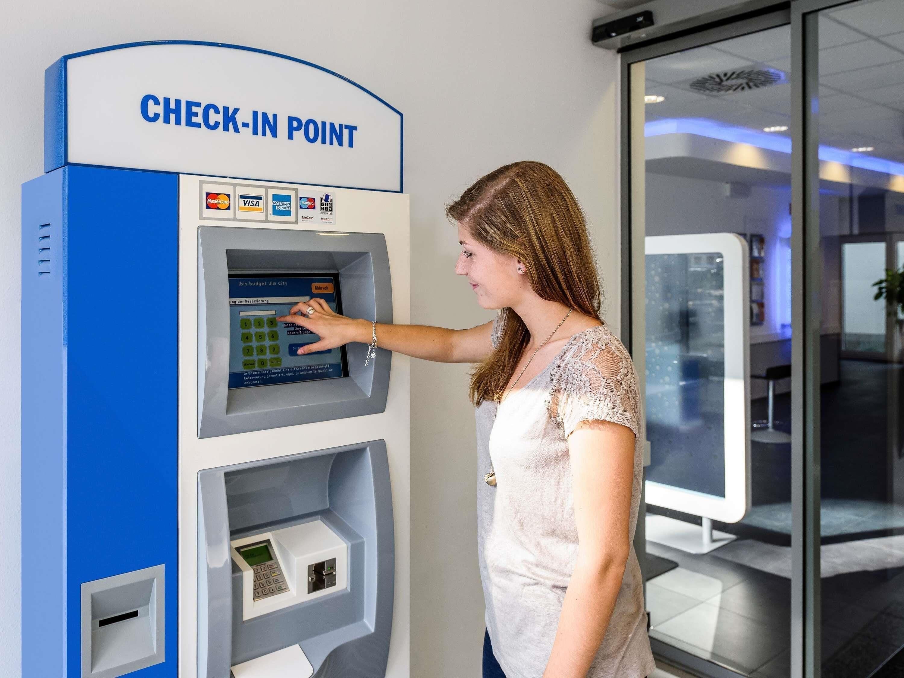 A woman using a check-in point with a digital interface, a card reader, and a cash slot.