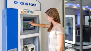 A woman using a check-in point with a digital interface, a card reader, and a cash slot.
