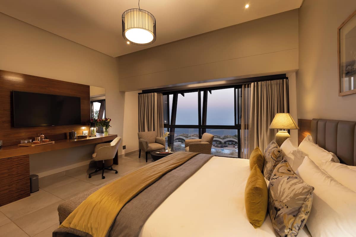 Habitación de hotel con una cama grande, un escritorio con televisor de pantalla plana, una silla, una lámpara y vistas a la ciudad.