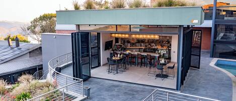 A modern outdoor bar area with a pool, surrounded by a glass enclosure, and a staircase leading to an upper level.