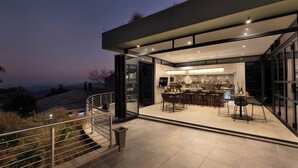 A modern kitchen with a bar area, large windows, and a staircase leading to an outdoor terrace.