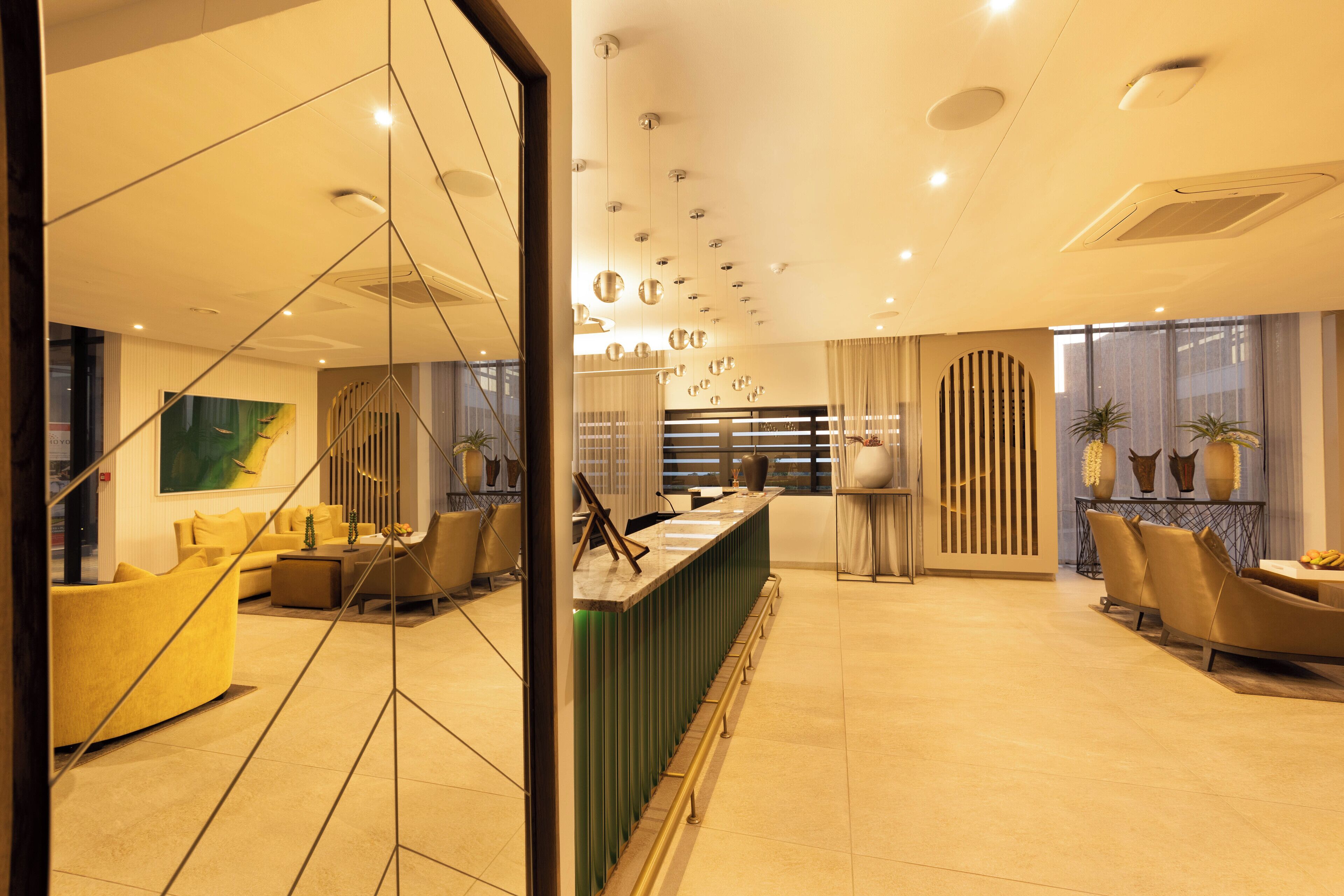 A modern hotel lobby with a reception desk, seating area, and large windows.