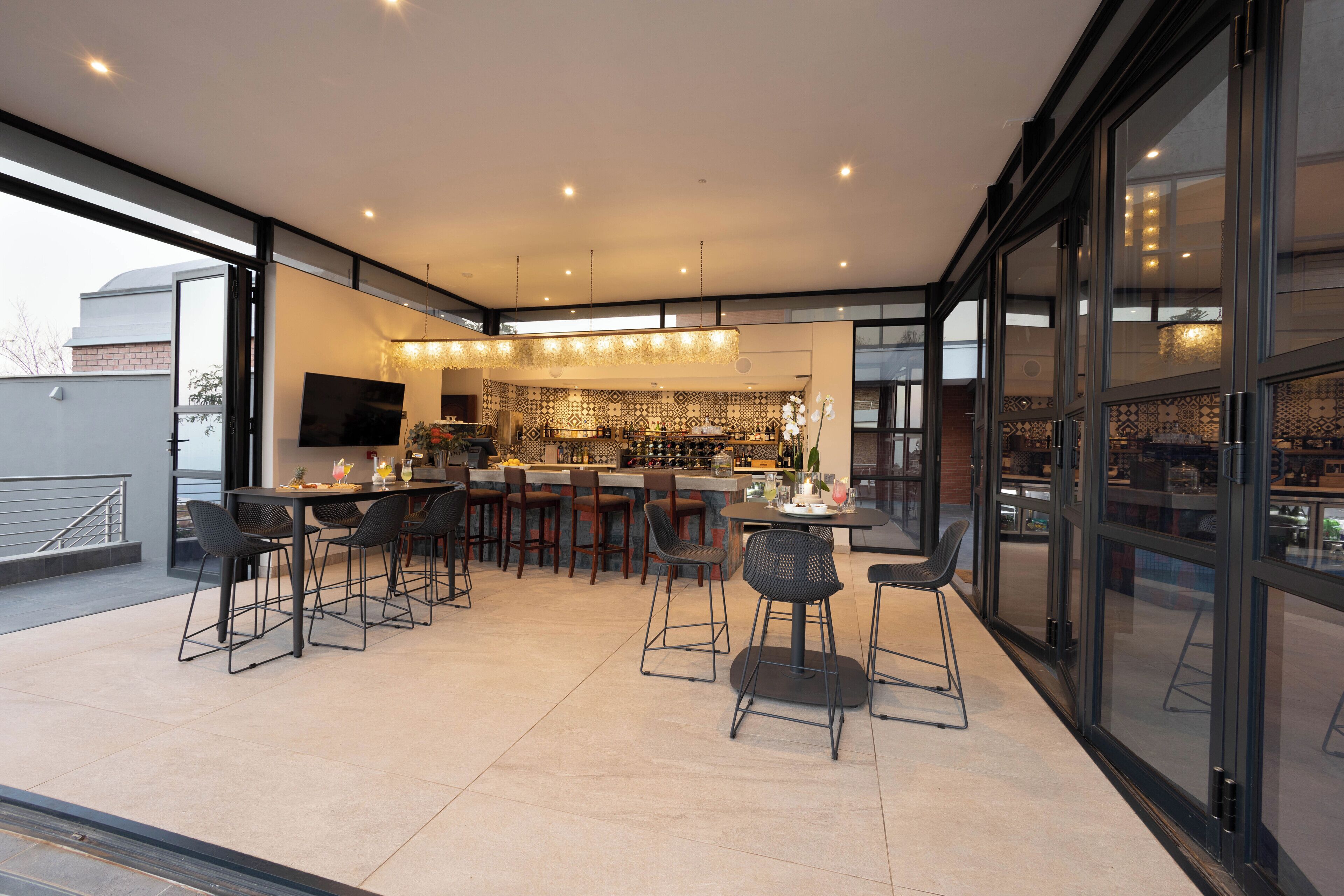 A modern kitchen with a bar area, large windows, and a dining space with chairs and tables.