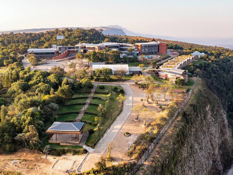 Um complexo moderno de edifícios com várias estruturas, rodeado por vegetação exuberante e um penhasco íngreme.
