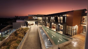 A modern hotel with a pool, outdoor seating, and a sunset view.