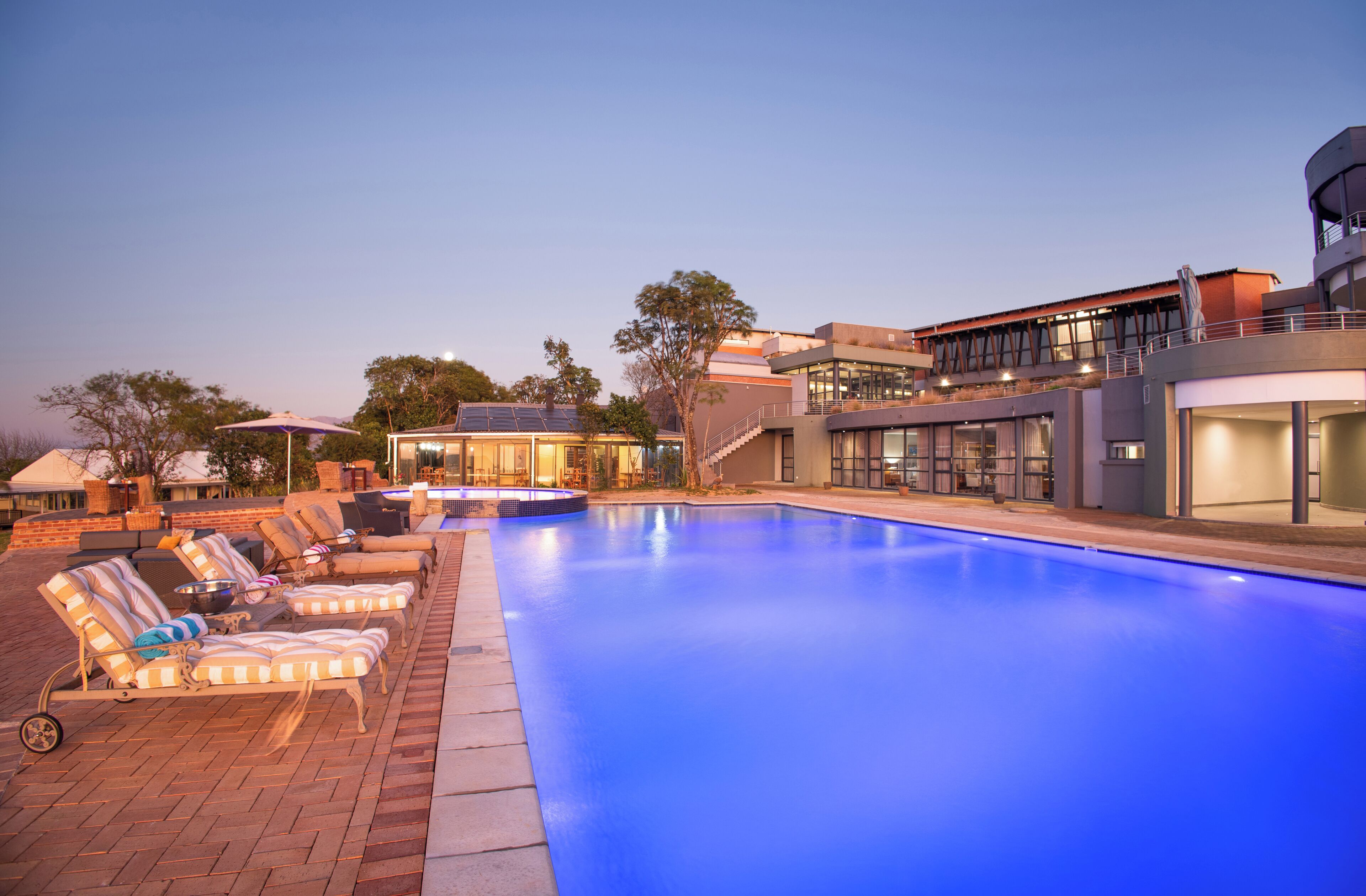 Une piscine avec des chaises longues et un bâtiment moderne doté de grandes fenêtres et d’un balcon.