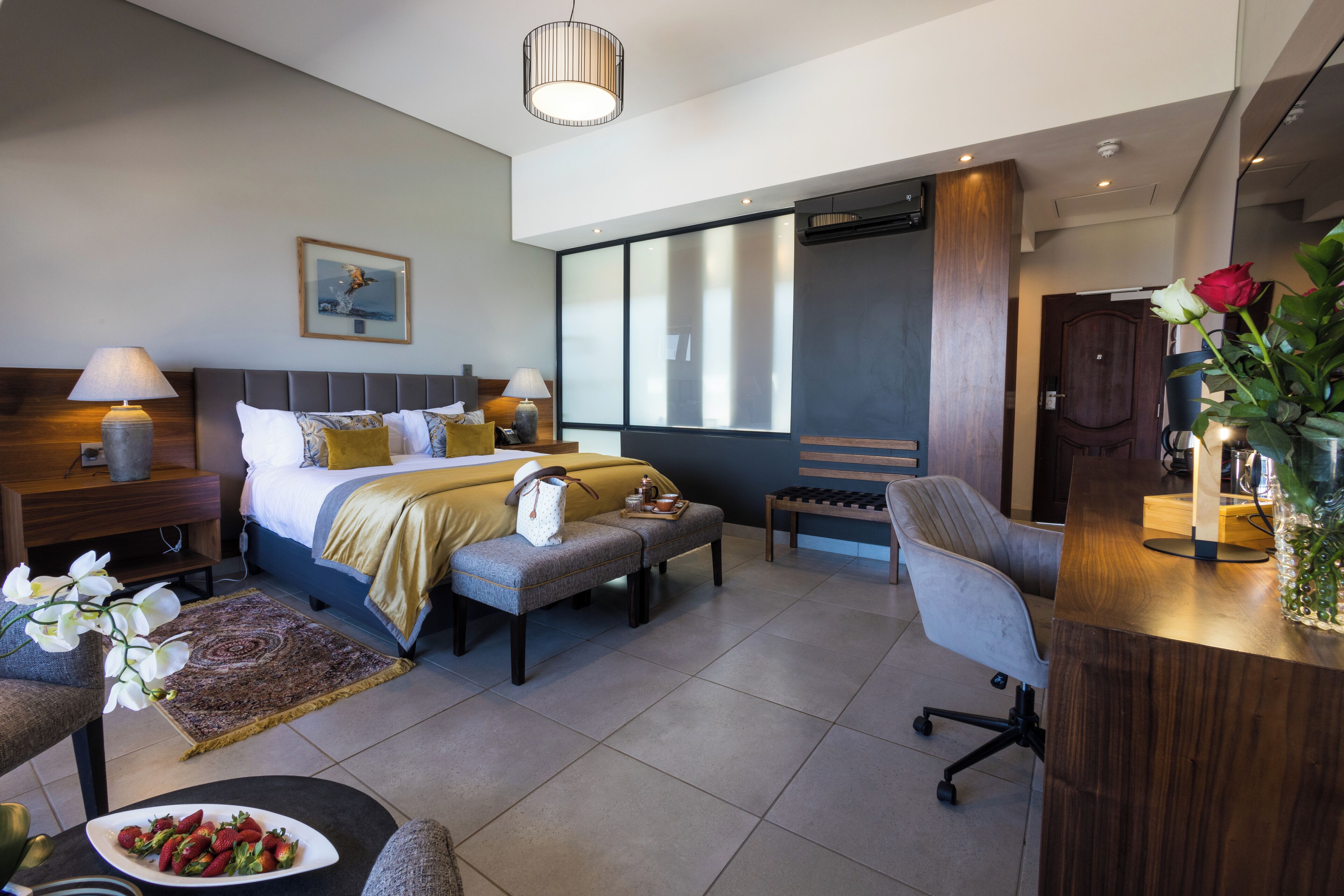 Une chambre d’hôtel moderne, équipée d’un lit, de tables de chevet, d’un bureau, d’une chaise, d’un tapis et d’un vase avec des fleurs.