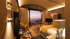 A hotel room with a large bed, a TV, a desk, and a view of the mountains.