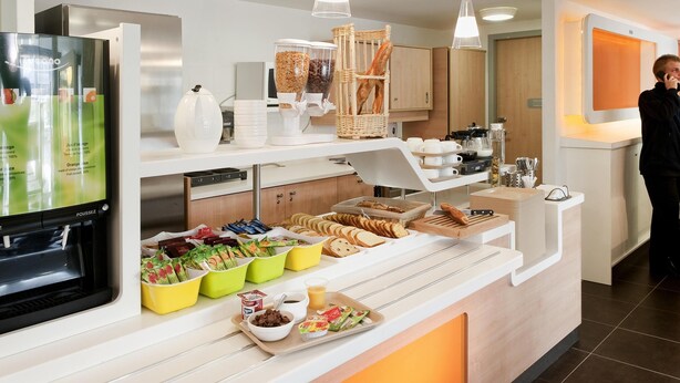 A buffet area with a variety of food items, a coffee machine, and a person standing by the counter.