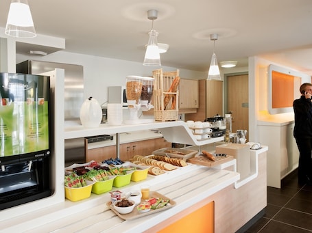 A buffet area with a variety of food items, a coffee machine, and a person standing by the counter.
