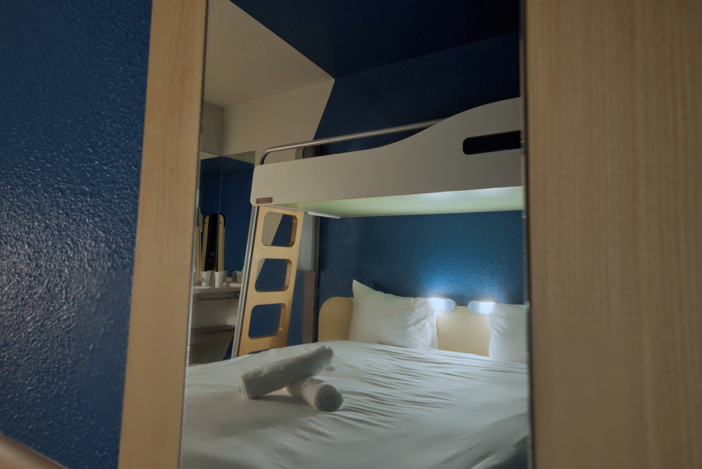 A bunk bed with a ladder, white bedding, and a headboard with built-in lighting.