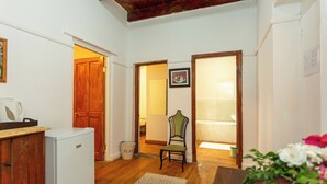 A compact room with a wooden floor, a white refrigerator, a chair, a wooden door, and a small rug. - Bella de Karoo (Oudtshoorn)