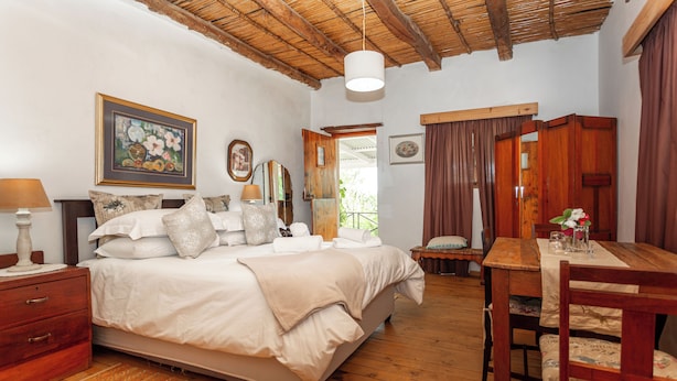 A bedroom with a bed, wooden floor, a dining table, and a chair. - Bella de Karoo (Oudtshoorn)