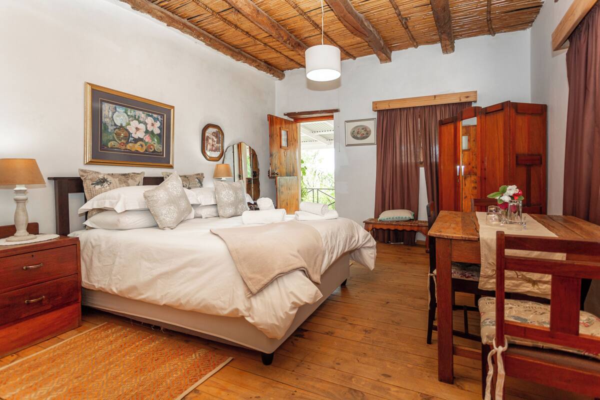 Un dormitorio con cama, suelo de madera, una mesa de comedor y una silla.