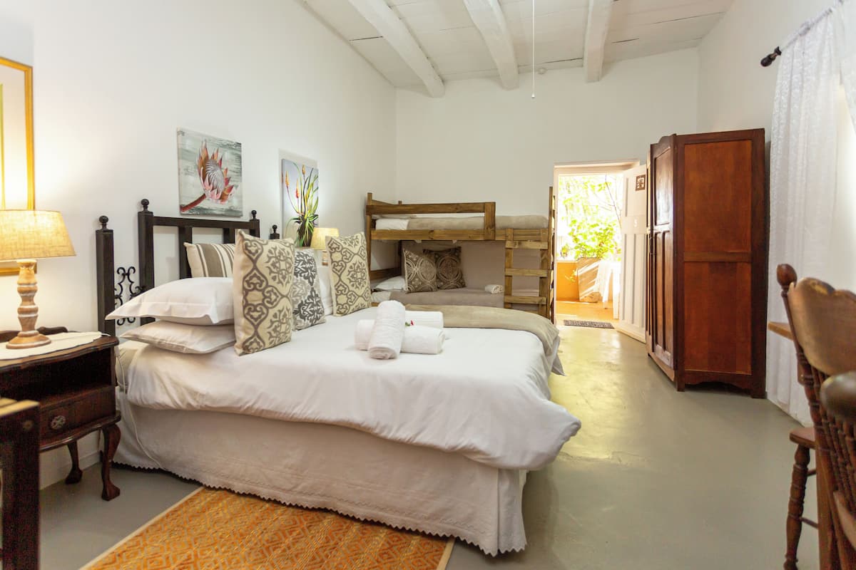 Un dormitorio con una cama litera, una mesita de noche con lámpara, un armario de madera y una puerta que da a otra habitación.
