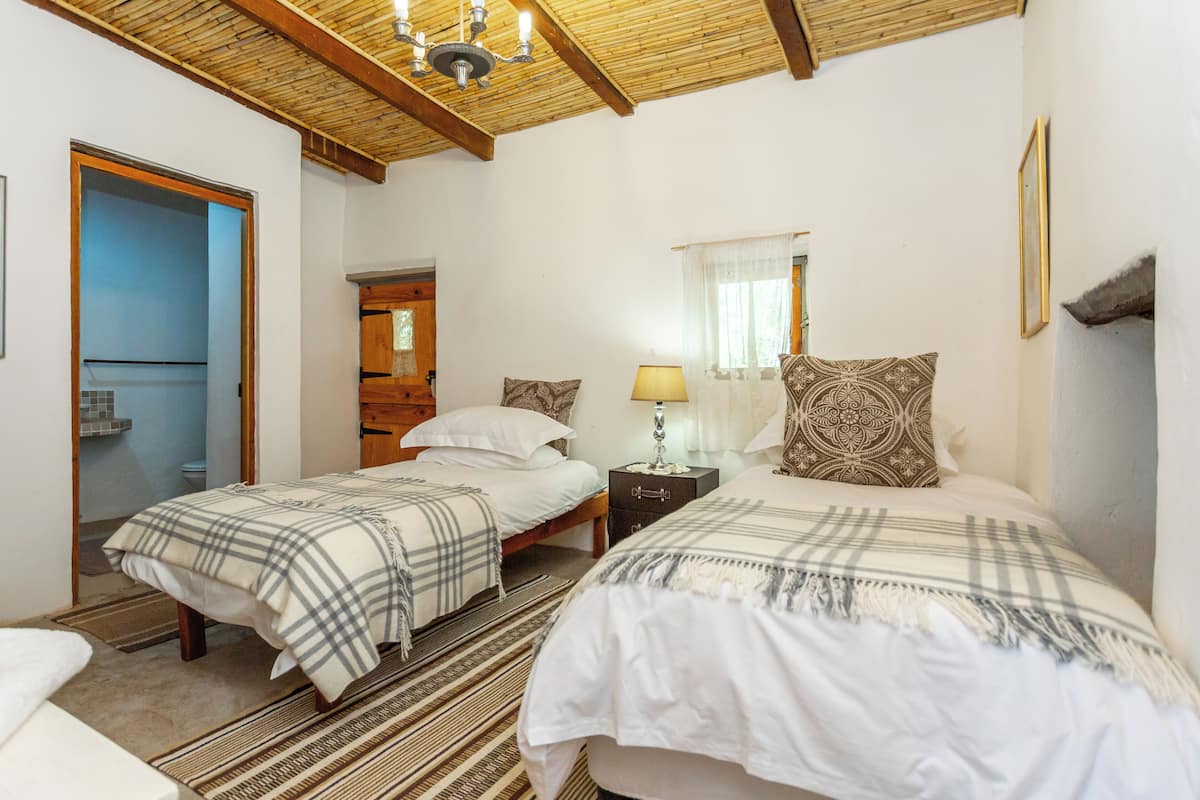Un dormitorio con dos camas, techo de madera, mesita de noche con lámpara y un espejo.