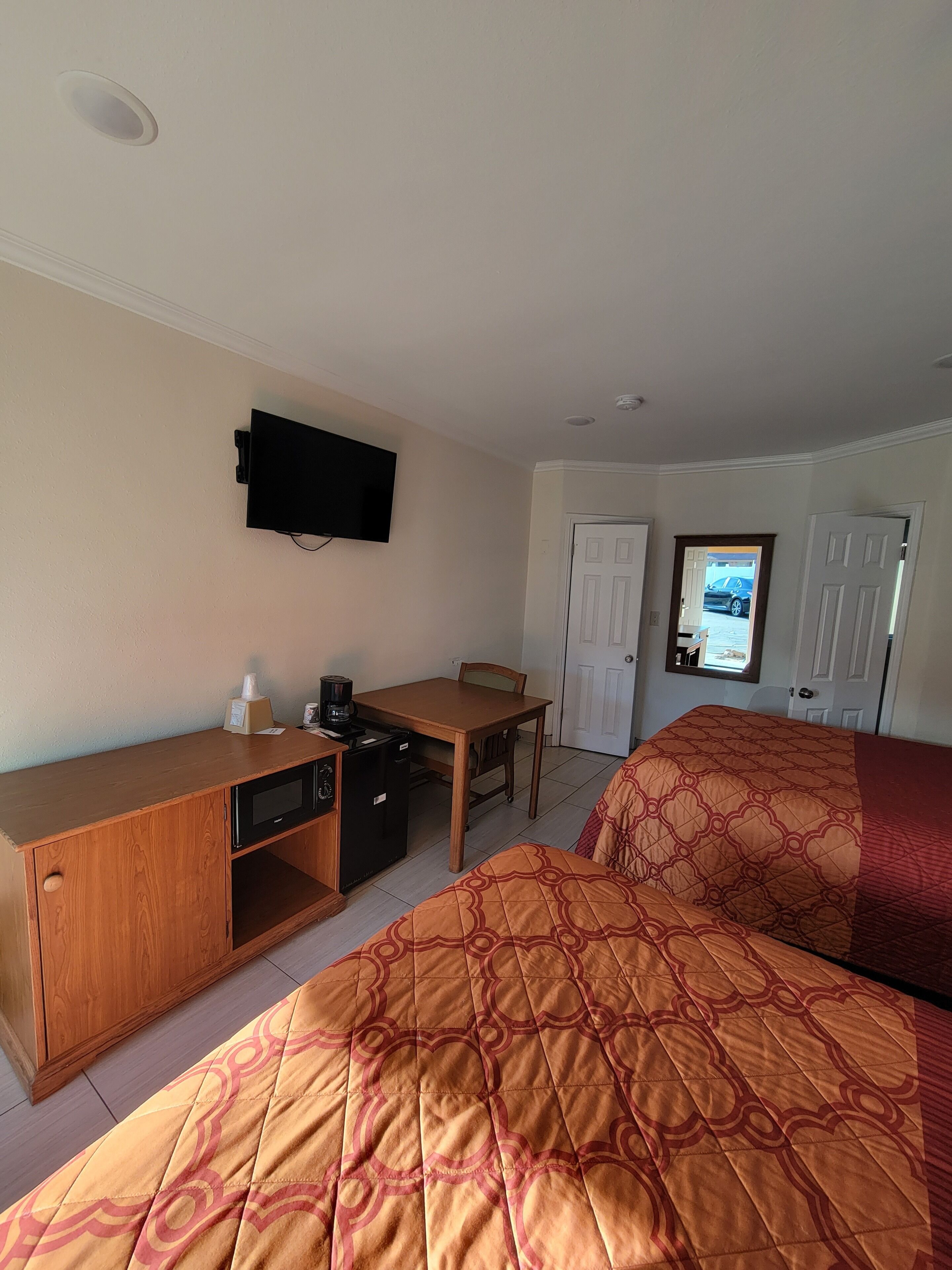 Habitación de hotel con una cama, un escritorio con computadora, televisión y puerta que da a un estacionamiento.