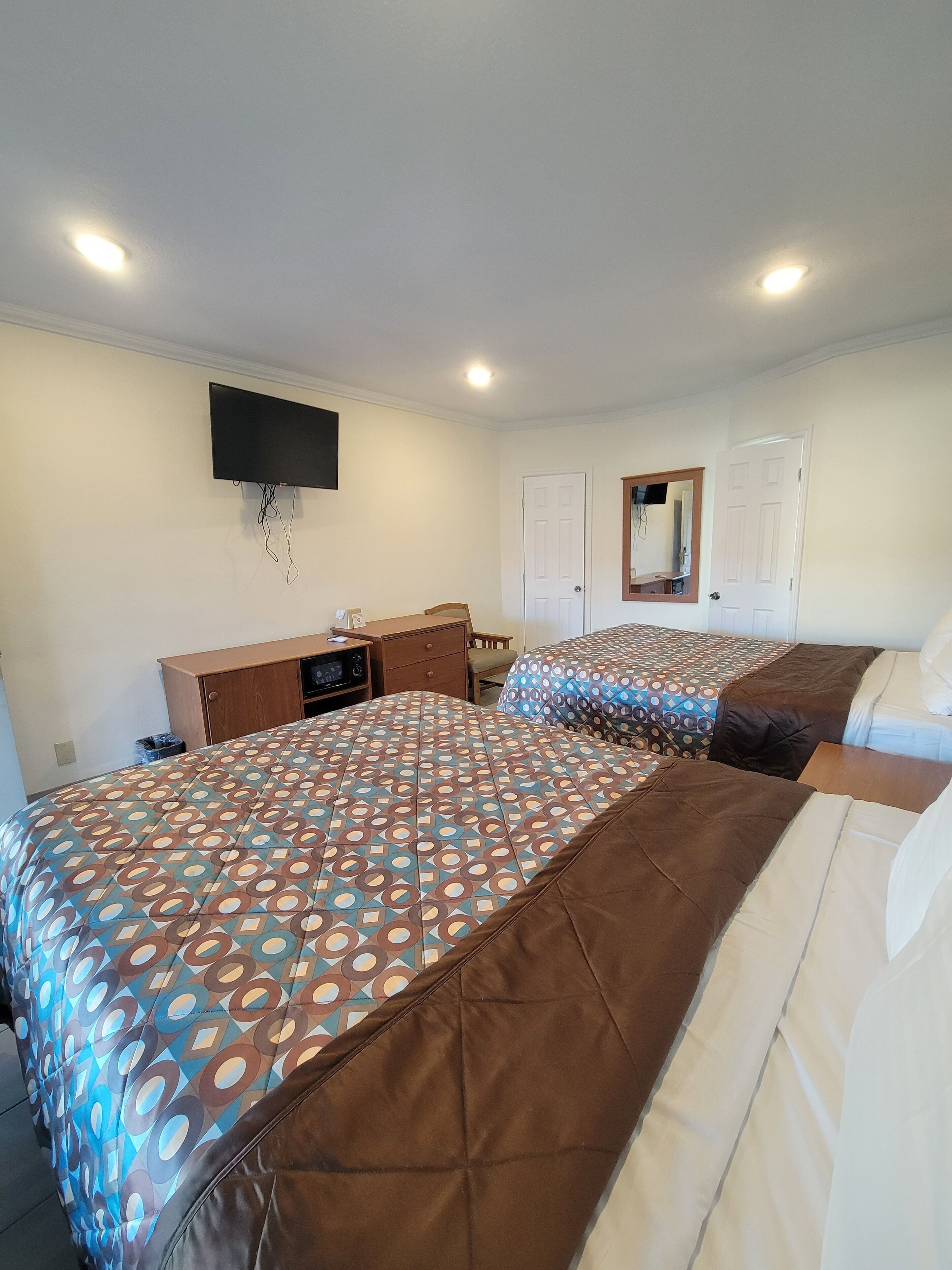 A bedroom with two beds, a TV mounted on the wall, and a desk with a chair.