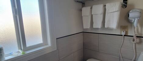 A bathroom with a toilet, a towel rack with multiple towels, a hairdryer, and a window with frosted glass.
