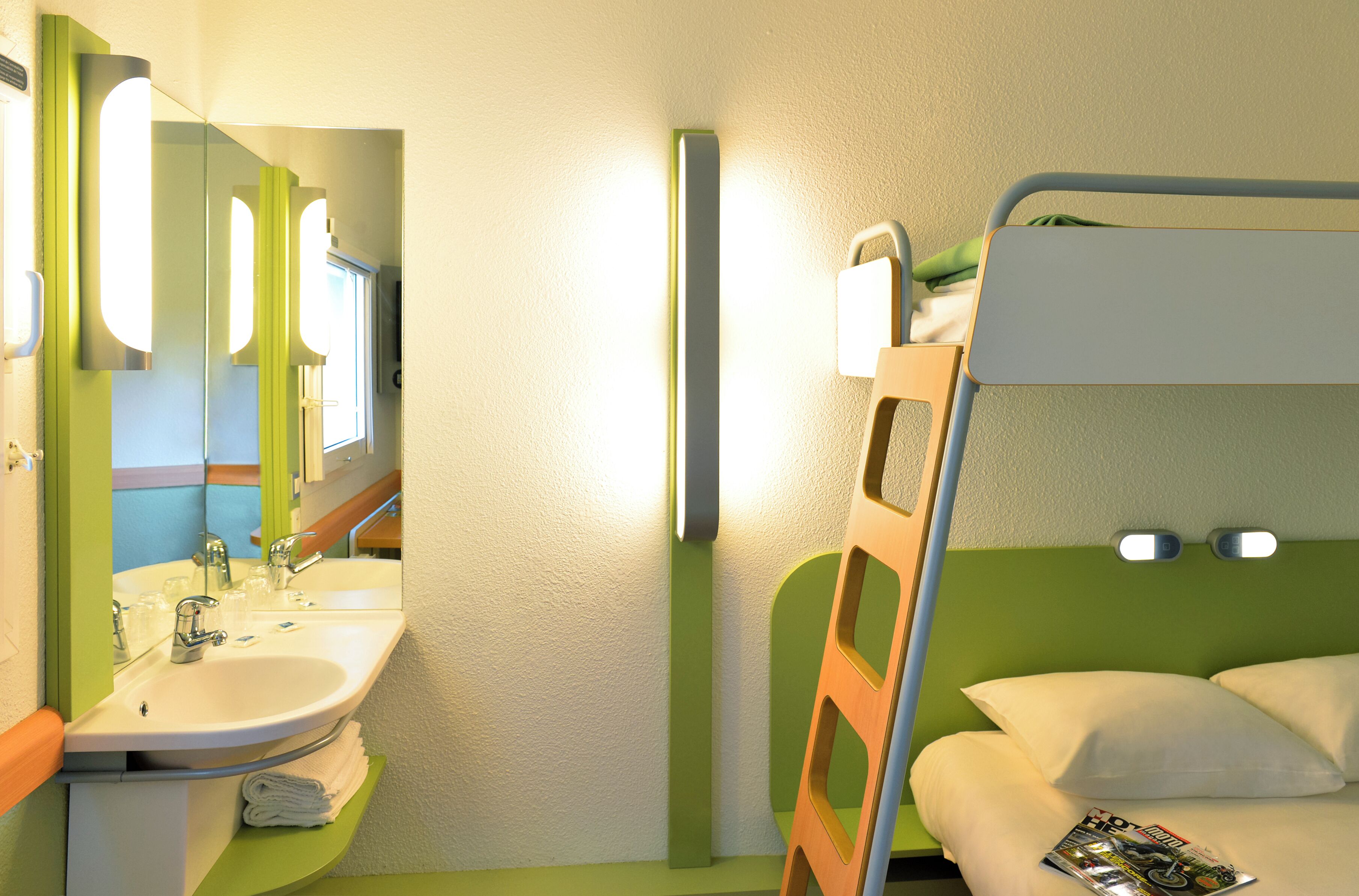 A compact hotel room with a bunk bed, a sink, and a mirror.