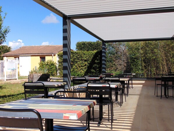 Un patio al aire libre con mesas y sillas, una zona de estar cubierta y un edificio al fondo.