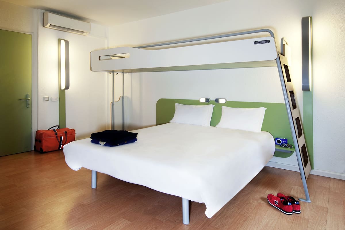 Un lit superposé avec une tête de lit verte, du linge de lit blanc, une valise et une paire de chaussures sur le sol.
