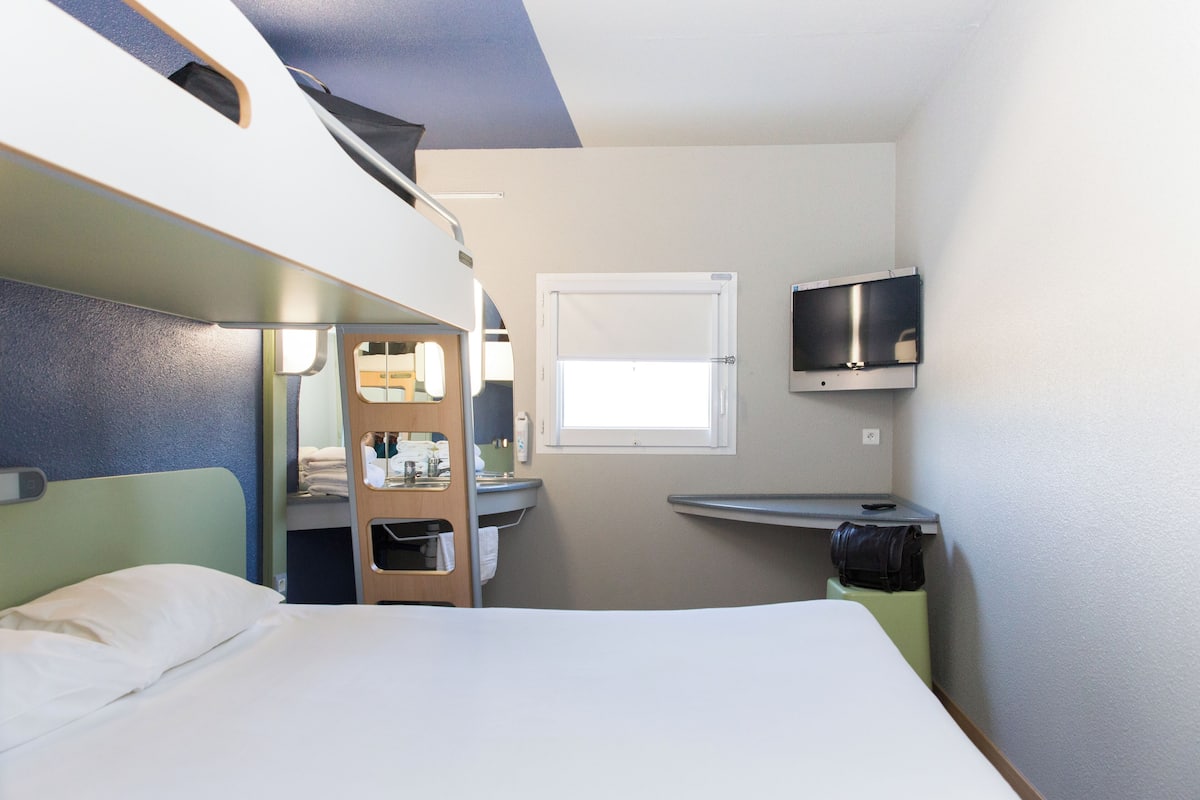 Una habitación de hotel pequeña con literas, un escritorio, televisión y ventana.