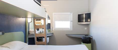 Ein kleines Hotelzimmer mit Stockbetten, einer kleinen Küchenzeile, einem Fernseher und einem Fenster.