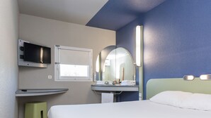 A hotel room with a bed, a TV mounted on the wall, a sink with a mirror, and a window.