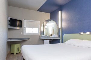 Habitación de hotel con cama, televisor montado en la pared, lavamanos con espejo y ventana.