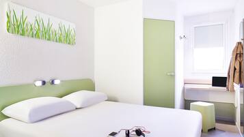 Een moderne slaapkamer met een bed, een nachtkastje met een laptop, een groene wanddecoratie en een raam met uitzicht.