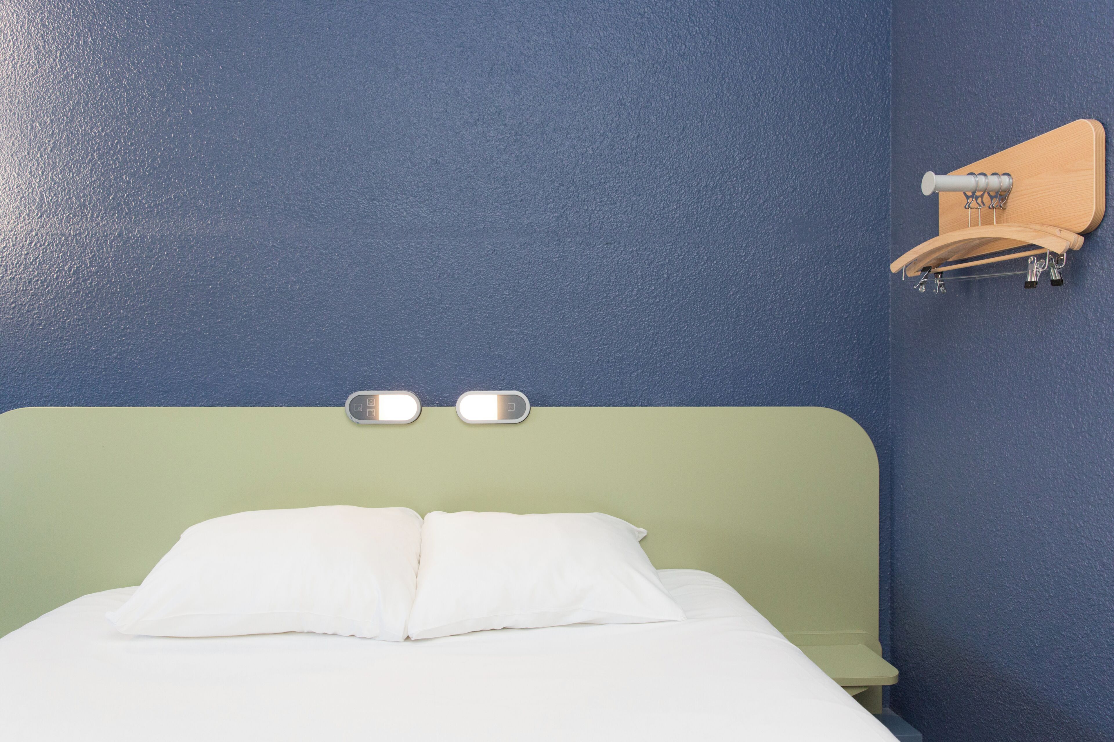 A bed with a green headboard, two bedside lamps, and a wooden shelf with a hook.