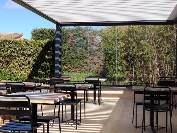 An outdoor patio with tables and chairs, surrounded by dense foliage and a clear sky. - ibis budget Sisteron (Sisteron)